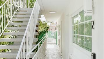 Un pasillo estrecho de paredes blancas con una escalera blanca a la izquierda y una ventana a la derecha.