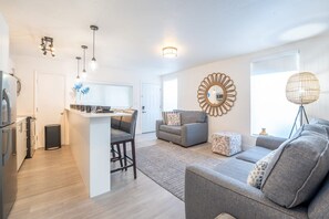 A modern living room with a grey sofa, a coffee table, and a dining area with a kitchen counter. - ONE Bedroom Apartment (Miami Beach)