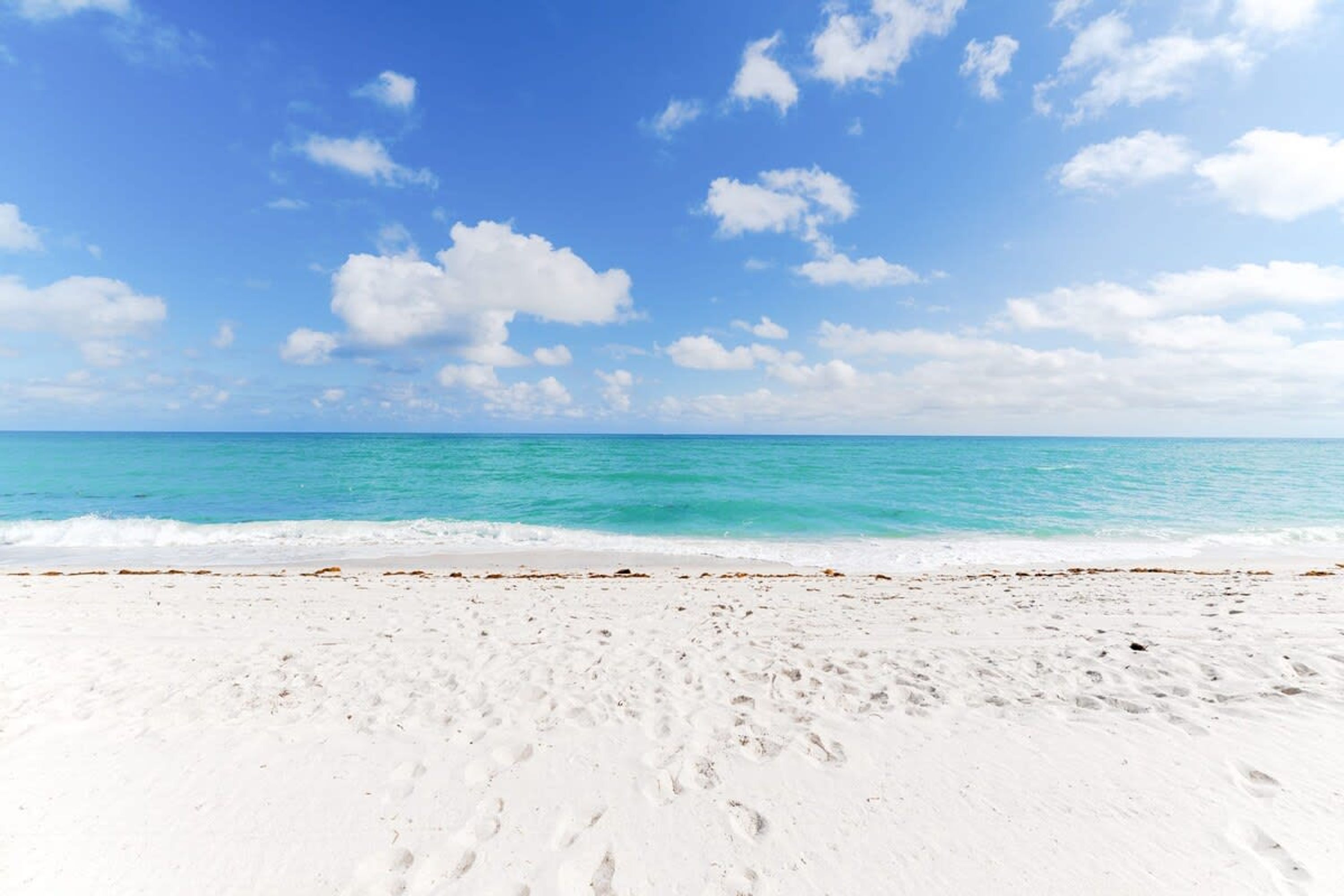 Une plage de sable blanc bordée d’une eau turquoise, sous un ciel bleu dégagé.