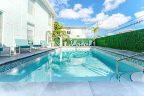 A swimming pool with a tiled edge, surrounded by lounge chairs and a green hedge. - ONE Bedroom Apartment (Miami Beach)