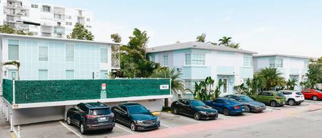 A parking lot with multiple cars, a green fence, and buildings with light blue exteriors.