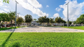 A volleyball court with a net, surrounded by a grassy area and trees.