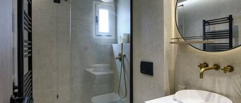 Un baño moderno con ducha de vidrio, lavamanos blanco y toallero empotrado.