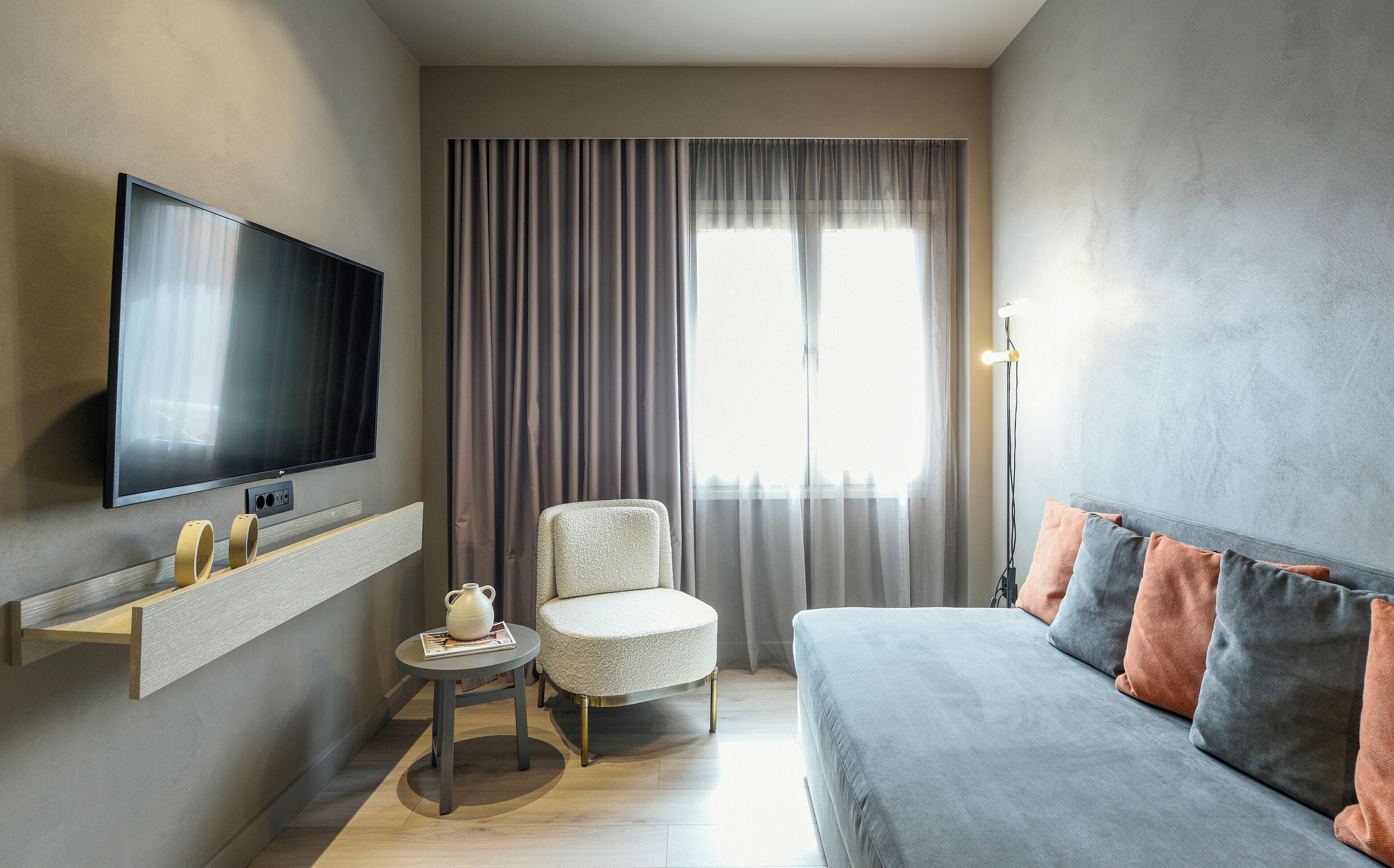A modern living room with a flat-screen TV, a round coffee table, a comfortable armchair, and a sofa with cushions.