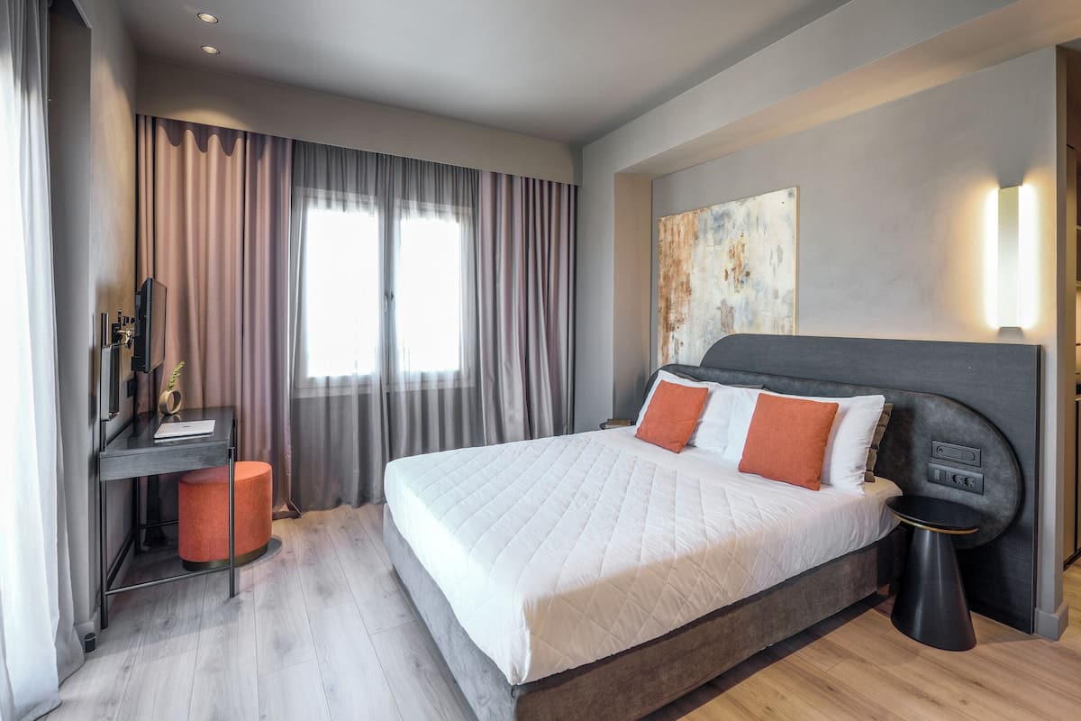 Habitación de hotel moderna con una cama grande, un escritorio con computadora y vista a la ciudad.