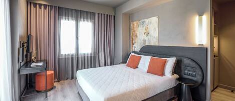 Habitación de hotel moderna con una cama grande, un escritorio con computadora y vista a la ciudad.
