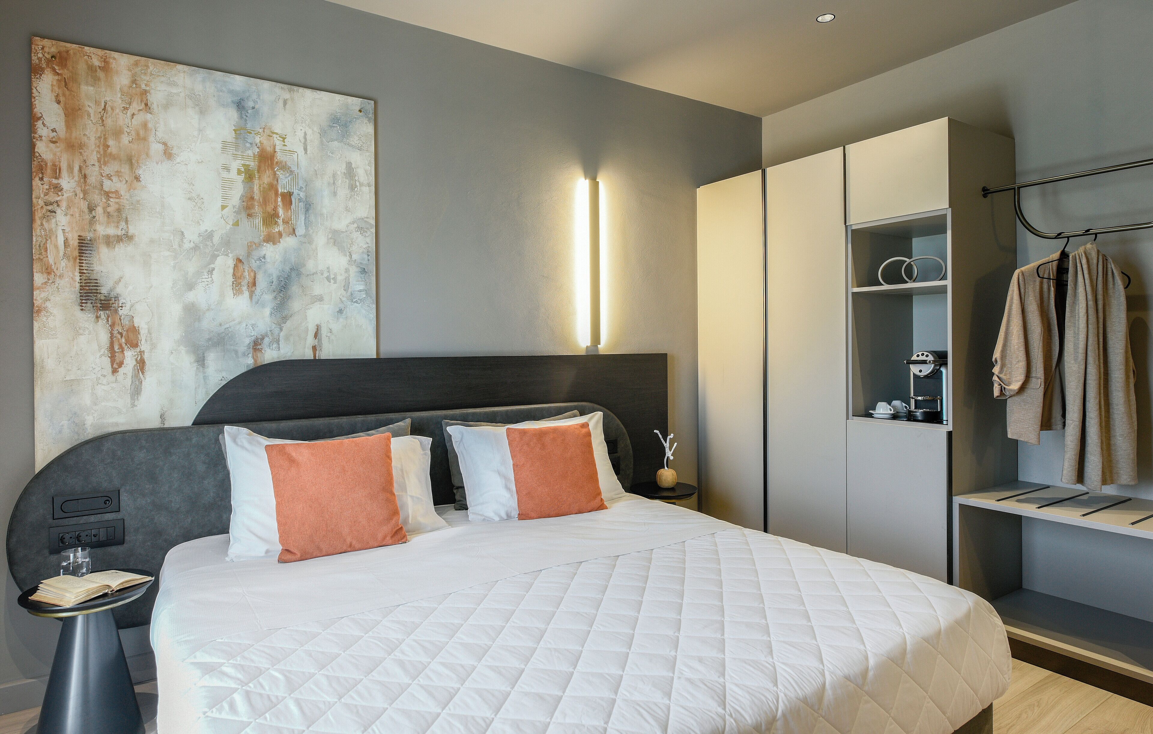 Un dormitorio moderno con una cama grande, mesitas de noche, un armario y una obra de arte en la pared.
