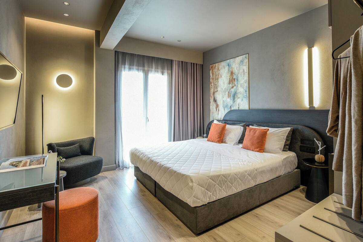 Una habitación de hotel moderna con una cama grande, un escritorio, una silla y un ventanal con cortinas.