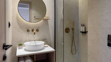 A modern bathroom with a glass-enclosed shower, a round mirror, a white sink, and neatly rolled towels.