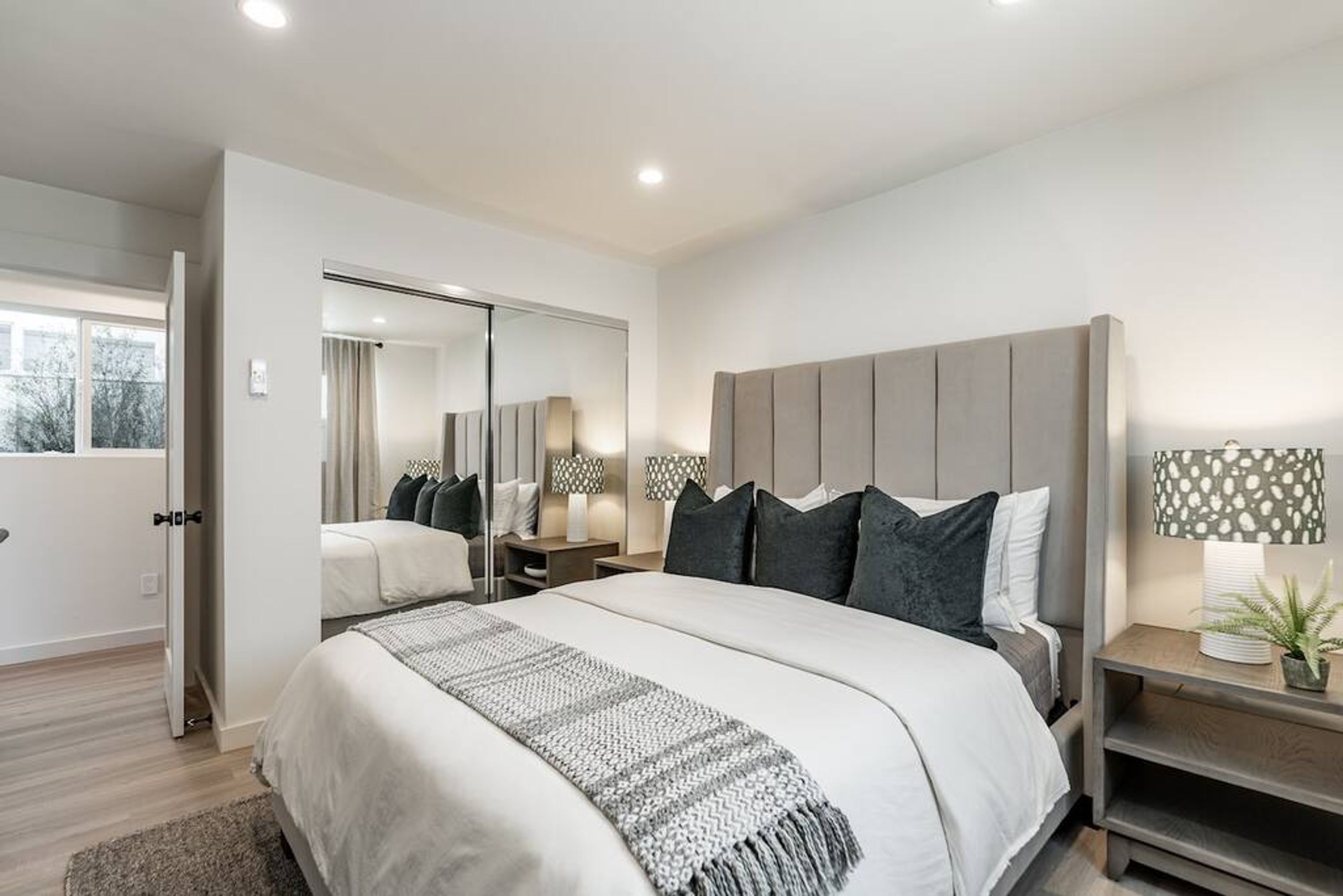 A modern bedroom with a large bed, a bedside table with a lamp, and a mirror on the wall.