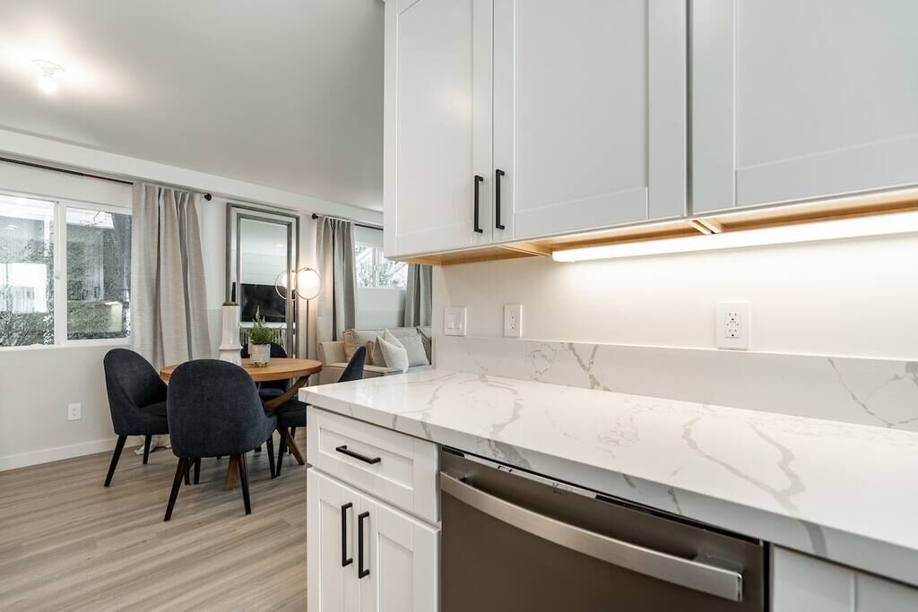 Uma cozinha moderna com armários brancos, bancada de mármore e máquina de lavar louça embutida.