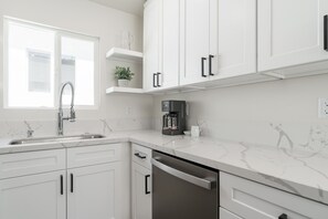 Een moderne keuken met witte kastjes, een roestvrijstalen vaatwasser, een koffiezetapparaat en een raam met uitzicht.