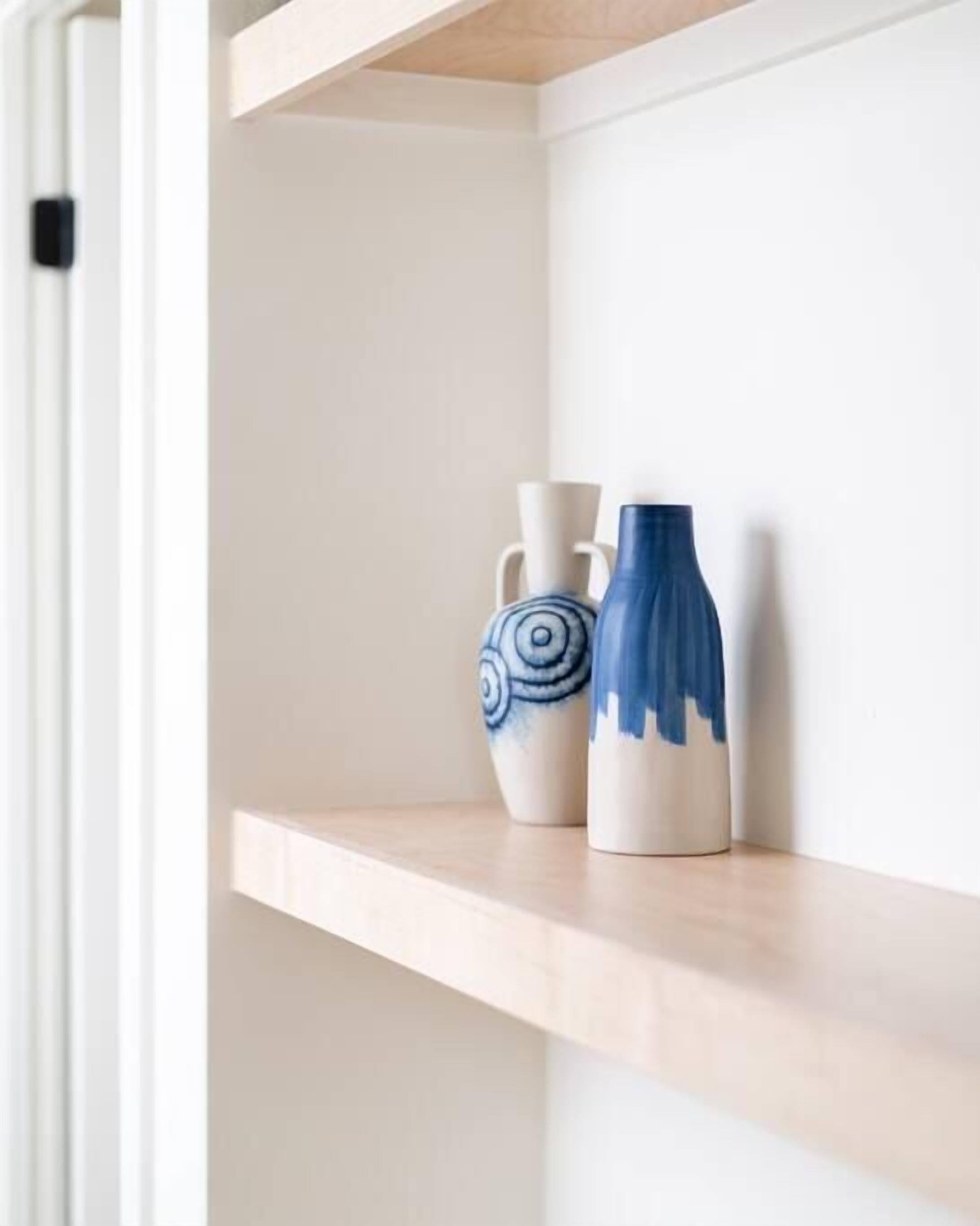 A shelf with two ceramic vases, one with a blue spiral design and the other with a blue abstract pattern.