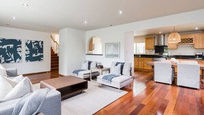 A spacious living area with a sofa, armchairs, and a coffee table. A kitchen is visible in the background with wooden cabinets and a dining area. - Ocean View Retreat- 4 Blocks From Solana Beach (Solana Beach)