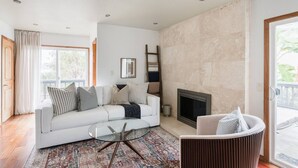 A modern living room with a white sofa, a glass coffee table, a patterned rug, a fireplace, and a view through a glass door. - Ocean View Retreat- 4 Blocks From Solana Beach (Solana Beach)