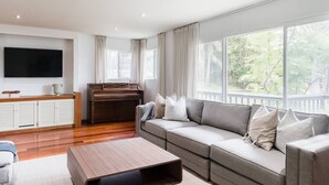 A modern living room with a sectional sofa, a wooden coffee table, a piano, and a TV mounted on the wall. - Ocean View Retreat- 4 Blocks From Solana Beach (Solana Beach)