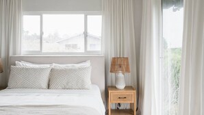 A bedroom with a bed, two pillows, a nightstand with a lamp, and a window with curtains. - Ocean View Retreat- 4 Blocks From Solana Beach (Solana Beach)