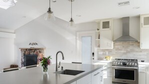 A modern kitchen with a large island, stainless steel appliances, and a stone fireplace. - Spacious and Bright 5-bedroom Oasis Pool and Yard (La Mesa)