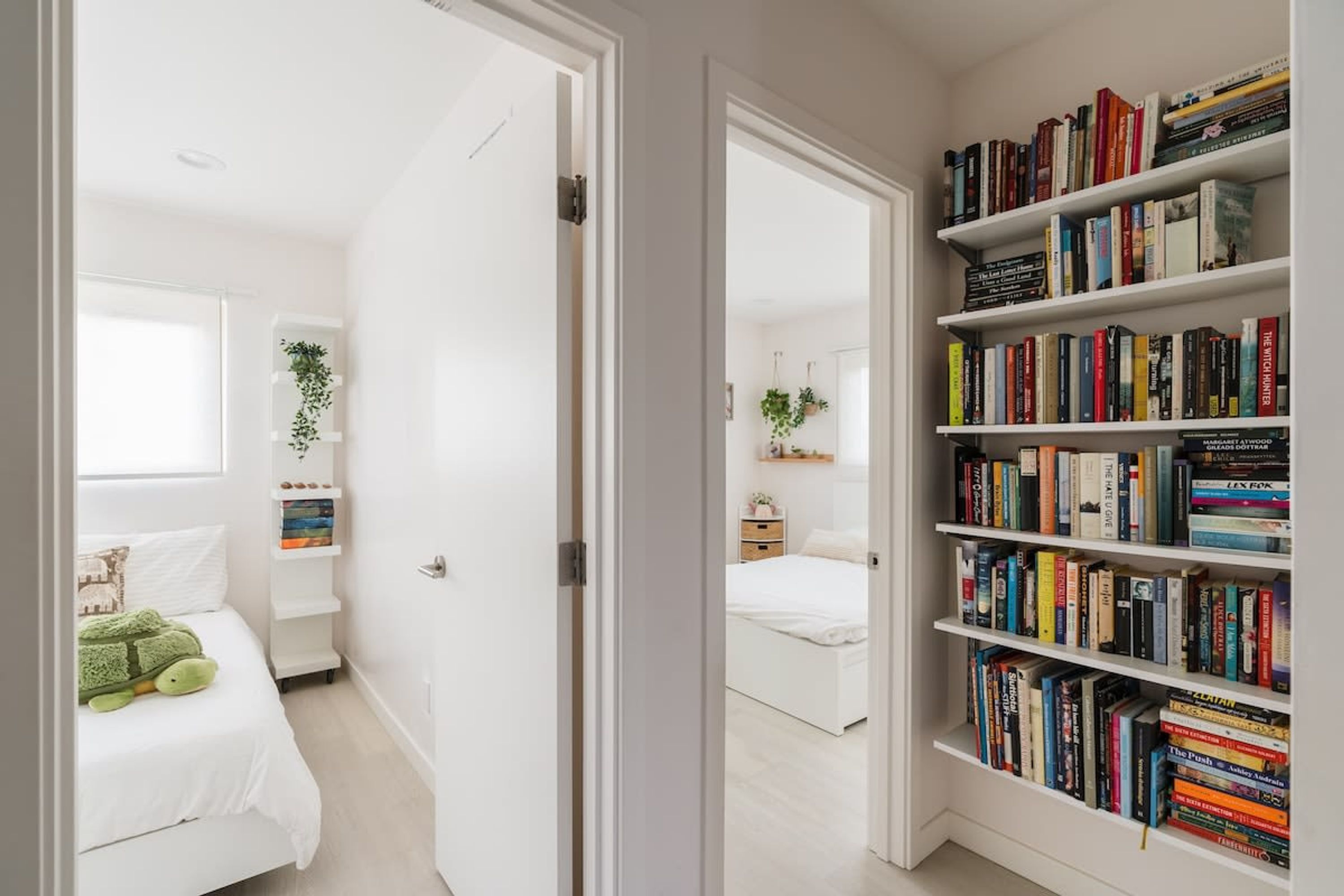A hallway with a bookshelf, a bed, and a window.