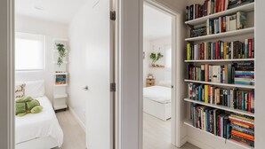 A hallway with a bookshelf, a bed, and a window. - Spacious and Bright 5-bedroom Oasis Pool and Yard (La Mesa)