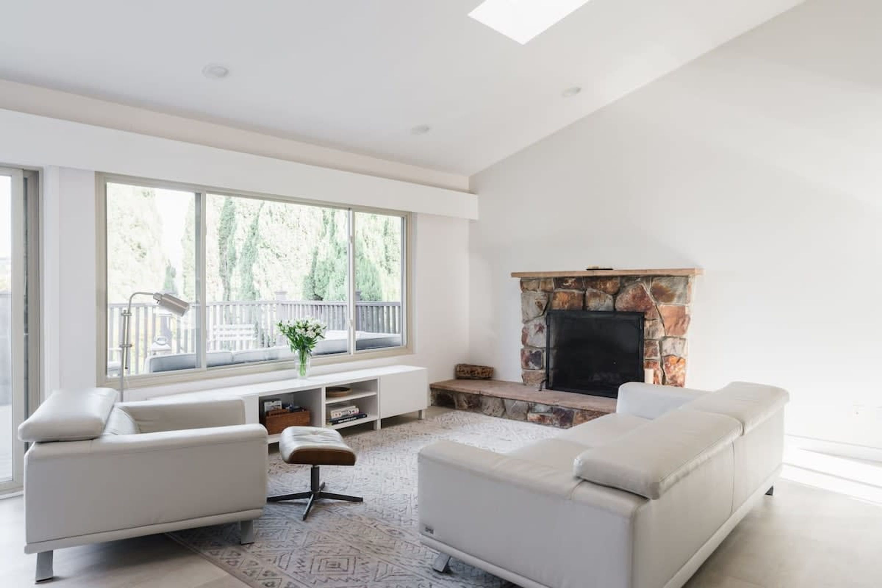 A spacious living room with a fireplace, large windows, and a balcony.