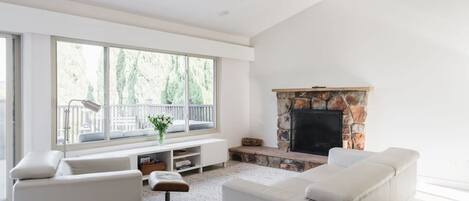 A spacious living room with a fireplace, large windows, and a balcony.