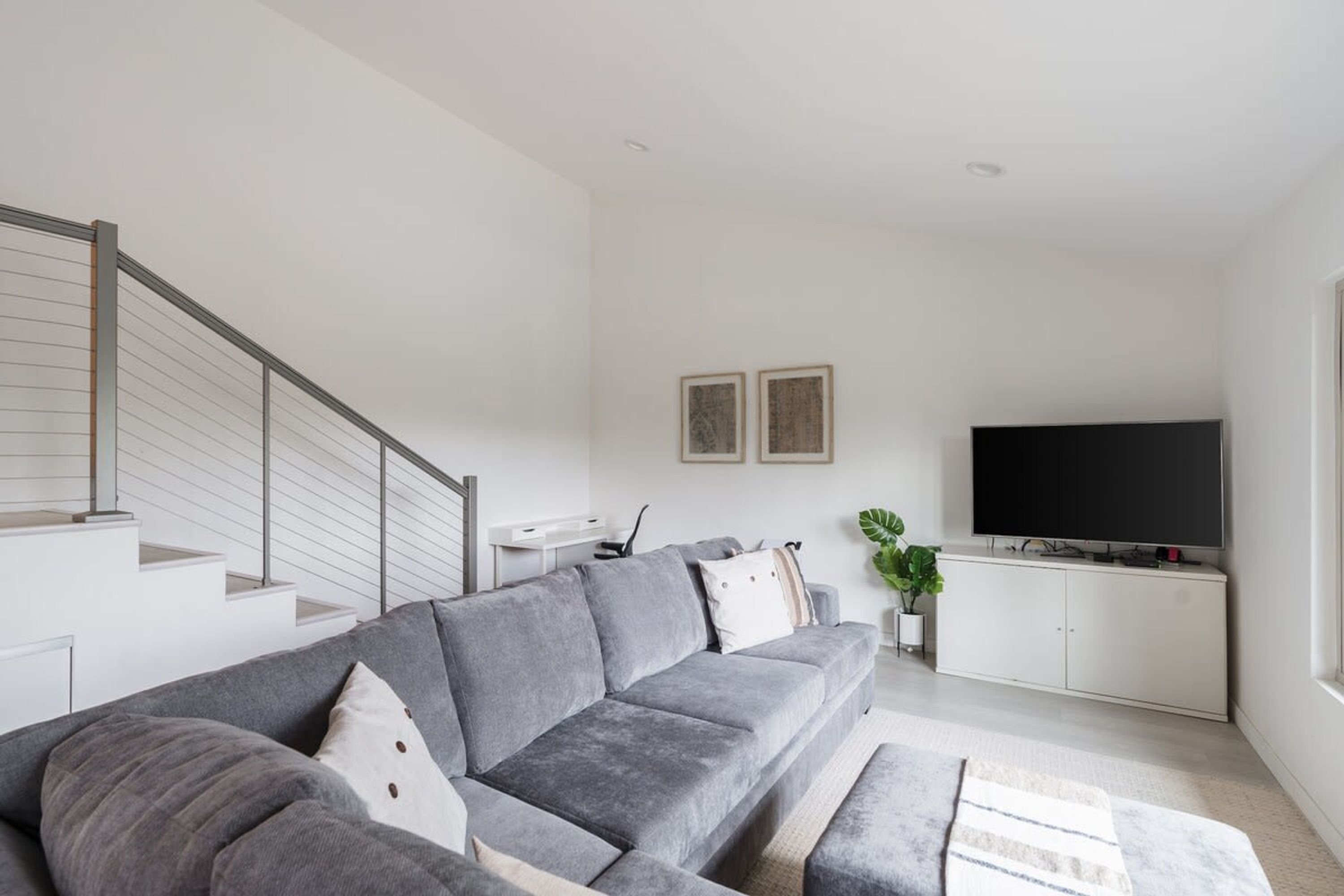 Un salon moderne avec un canapé d’angle gris, un téléviseur à écran plat et un escalier.