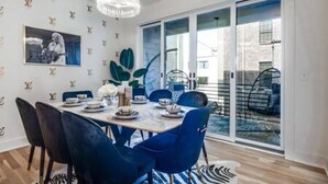 A dining area with a table set for four, blue chairs, a chandelier, and a large window with a view of the outdoors. - Music Fame House Gulch 4 Patios View Karaoke (Nashville)