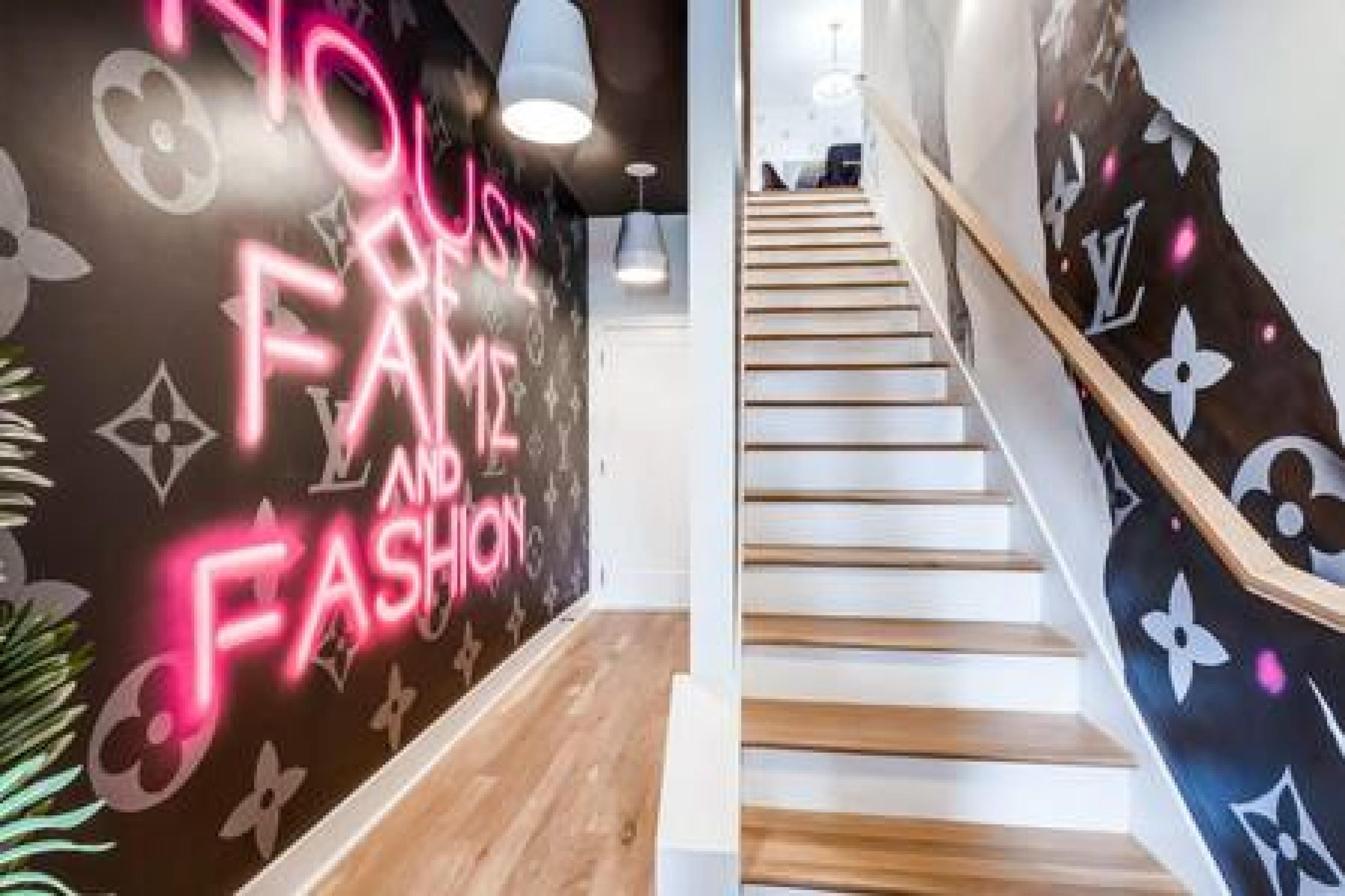 A staircase with a wooden handrail and a wall with a neon sign that reads "NO FAM AND FASHION".