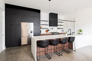 A modern kitchen with a large island, black bar stools, and stainless steel appliances.
