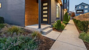A modern two-story house with a wooden front porch, a concrete pathway, and a well-maintained garden. - Nash Chic Near DT Rooftop Luxe Comfort (Nashville)