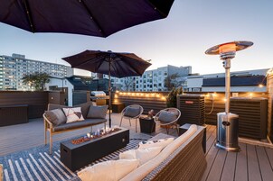 A rooftop patio with outdoor furniture, a heater, and string lights.