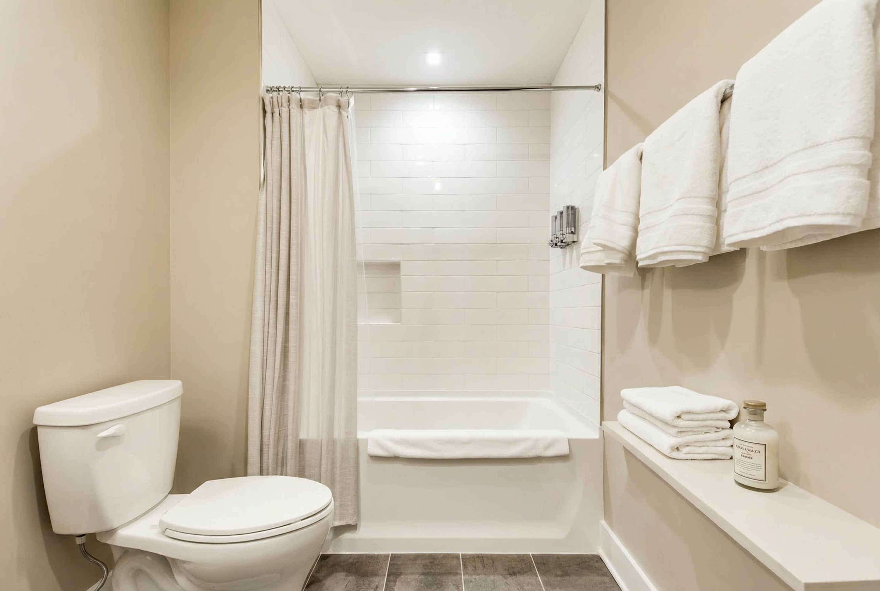 A bathroom with a toilet, shower, and bathtub. There are towels and a bottle on a shelf.