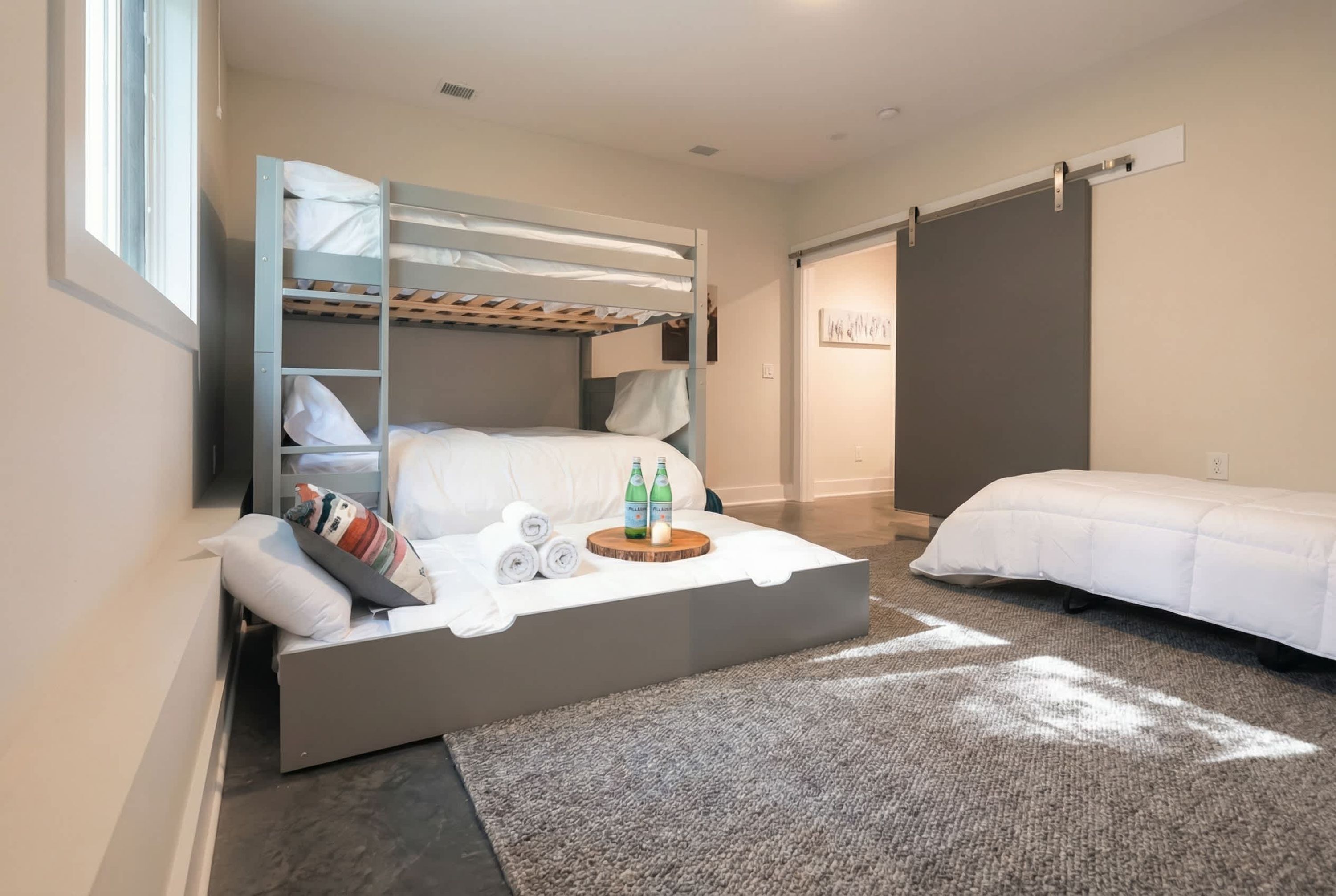 A bedroom with a bunk bed, a pull-out sofa, a small table with bottles, and a window.