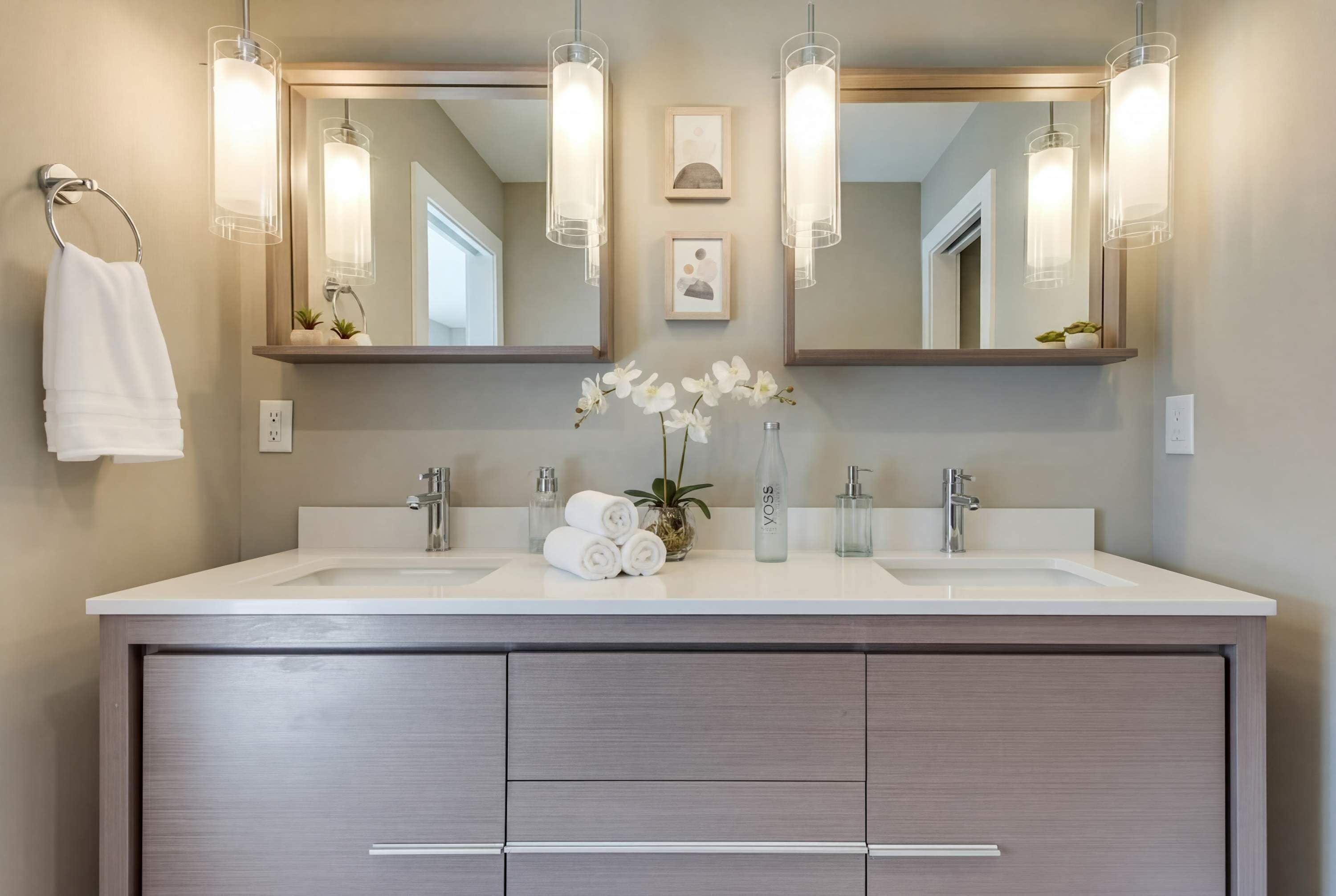 A modern bathroom with two sinks, a large mirror, pendant lights, and a towel rack.