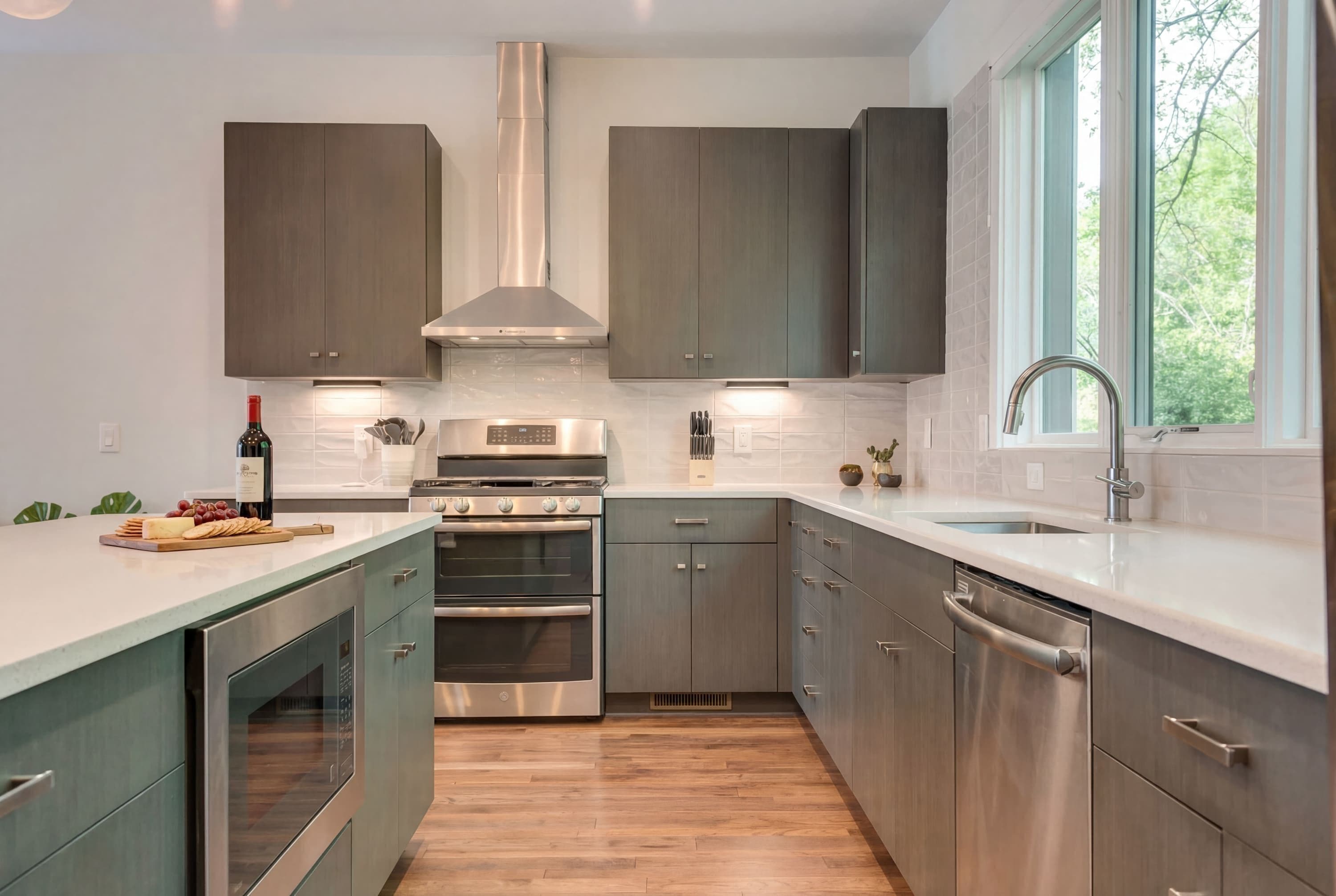 A modern kitchen with stainless steel appliances, grey cabinetry, and a large window providing natural light.