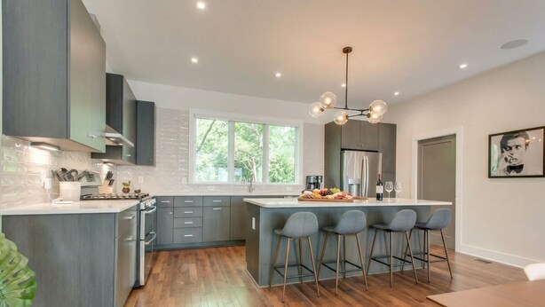 A modern kitchen with a central island, bar stools, and a large window.