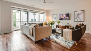 A spacious living room with hardwood floors, a large window, a ceiling fan, and a modern sofa.