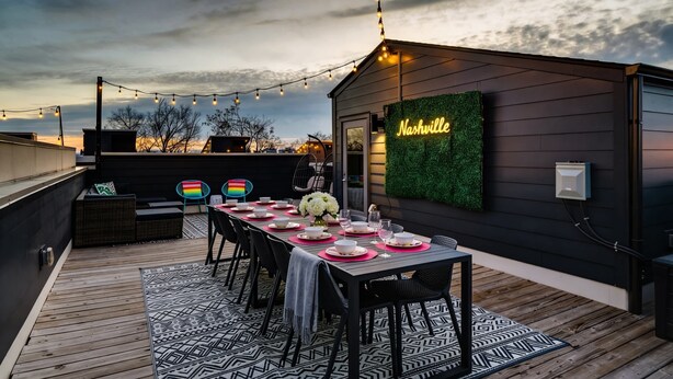 En tagterrasse med et langt spisebord dækket til seks personer, omgivet af sorte stole. En neonskilte på væggen viser ordet "Nashville".