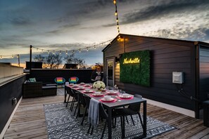 A rooftop patio with a long dining table set for six, surrounded by black chairs. A neon sign reads "Nashville" on the wall. - NEW Pink Howdy Oasis 13 Beds Rooftop View Parking (Nashville)