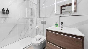 Un baño moderno con cabina de ducha de vidrio, inodoro blanco y tocador con espejo.