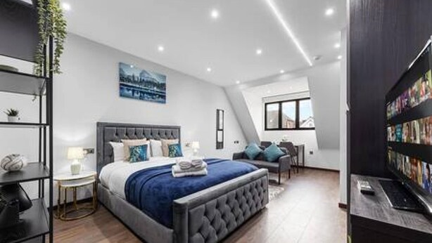 Un dormitorio moderno con una cama grande, un escritorio pequeño, una estantería y una ventana con vistas a la ciudad.