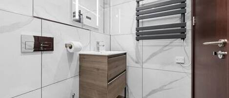 Un baño moderno con azulejos blancos, un tocador de madera, un perchero para toallas y un inodoro.