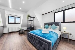 Quarto moderno com uma cama grande, uma mesinha de cabeceira, uma pequena mesa e uma janela.