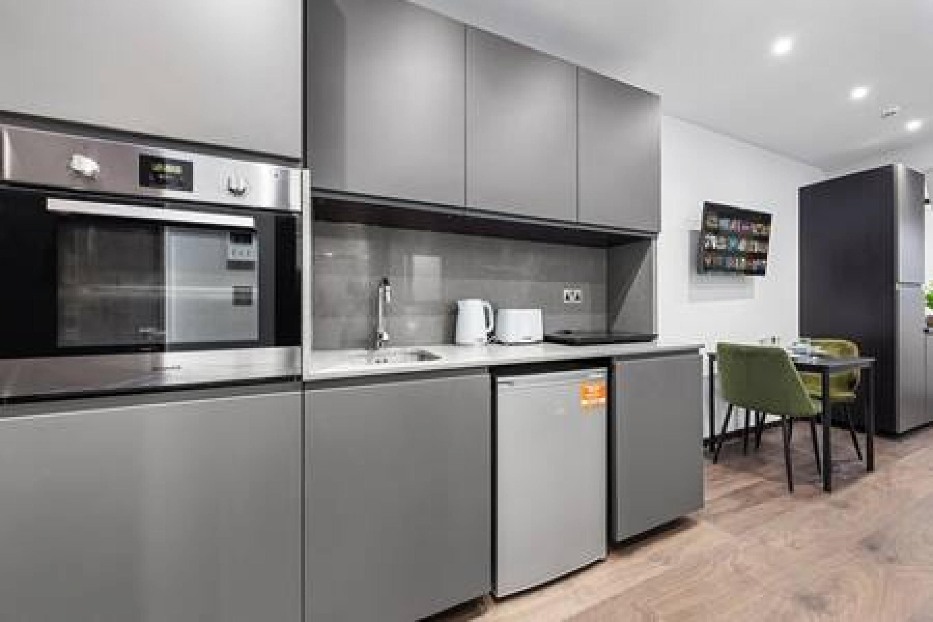 Eine moderne Küche mit Edelstahlgeräten, grauen Schränken und einem Essbereich mit Tisch und Stühlen.