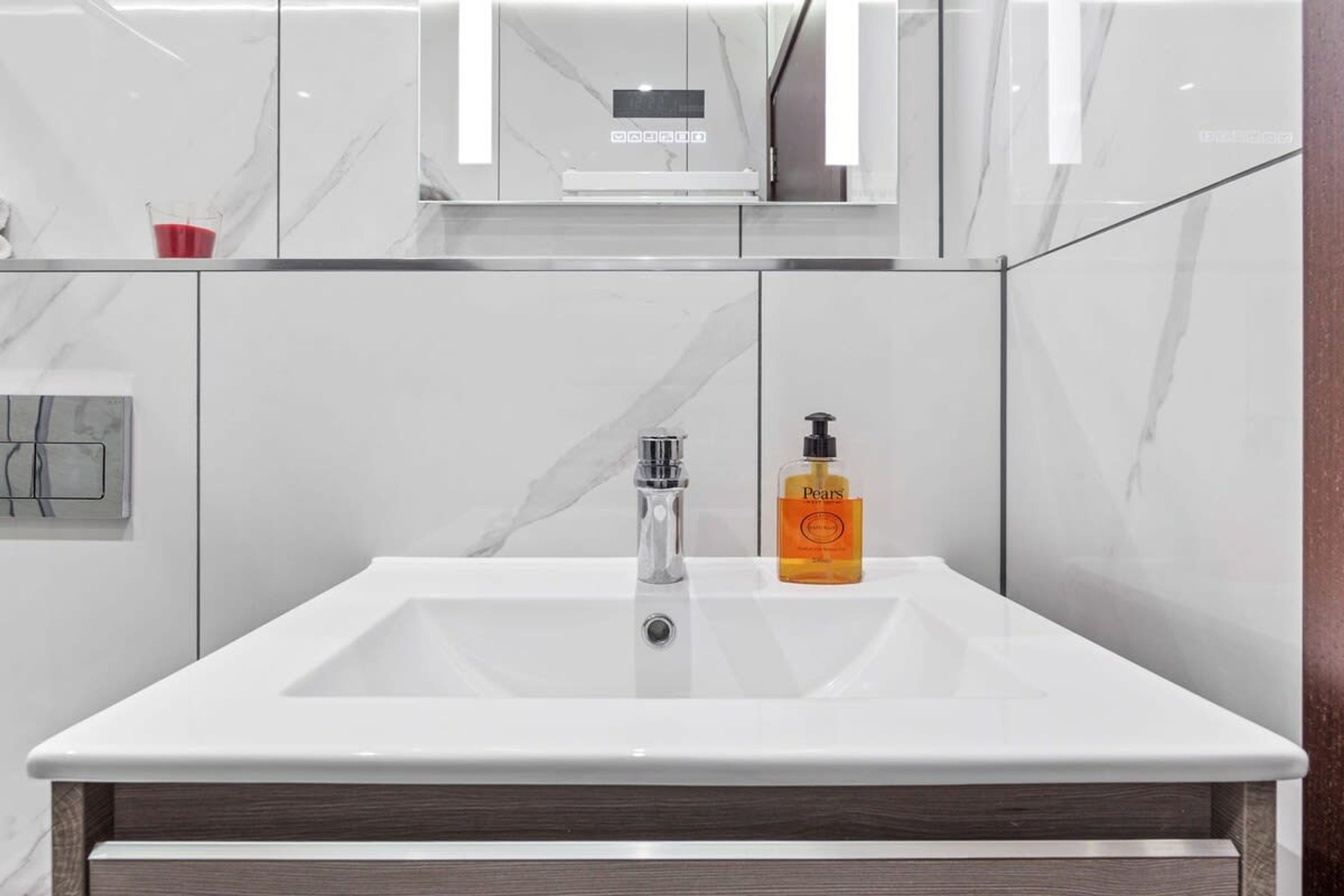 A modern bathroom with a white sink, a mirror above it, and a bottle of Pears lotion on the counter.