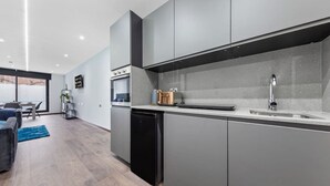 Une cuisine moderne avec des meubles gris, un lave-vaisselle noir et un évier en acier inoxydable.