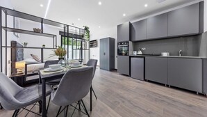 Eine moderne Küche mit grauen Schränken, eine Essecke mit Tisch und Stühlen sowie ein großes Fenster mit Pflanzen.