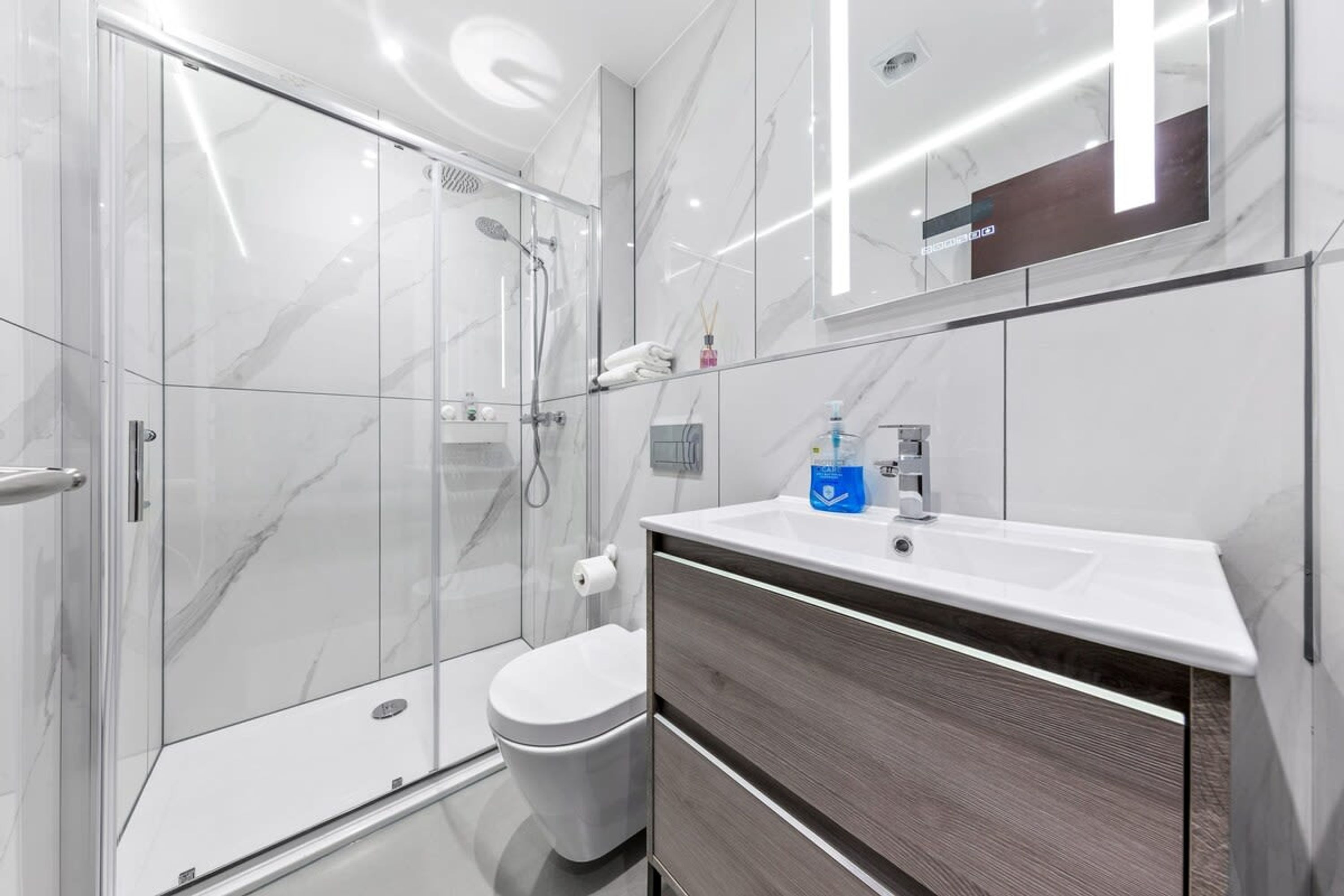 A modern bathroom with a glass shower enclosure, a white toilet, and a vanity with a mirror.