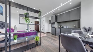 A modern kitchen with built-in appliances, a dining area with a table and chairs, and a living area with a sofa and decorative plants.